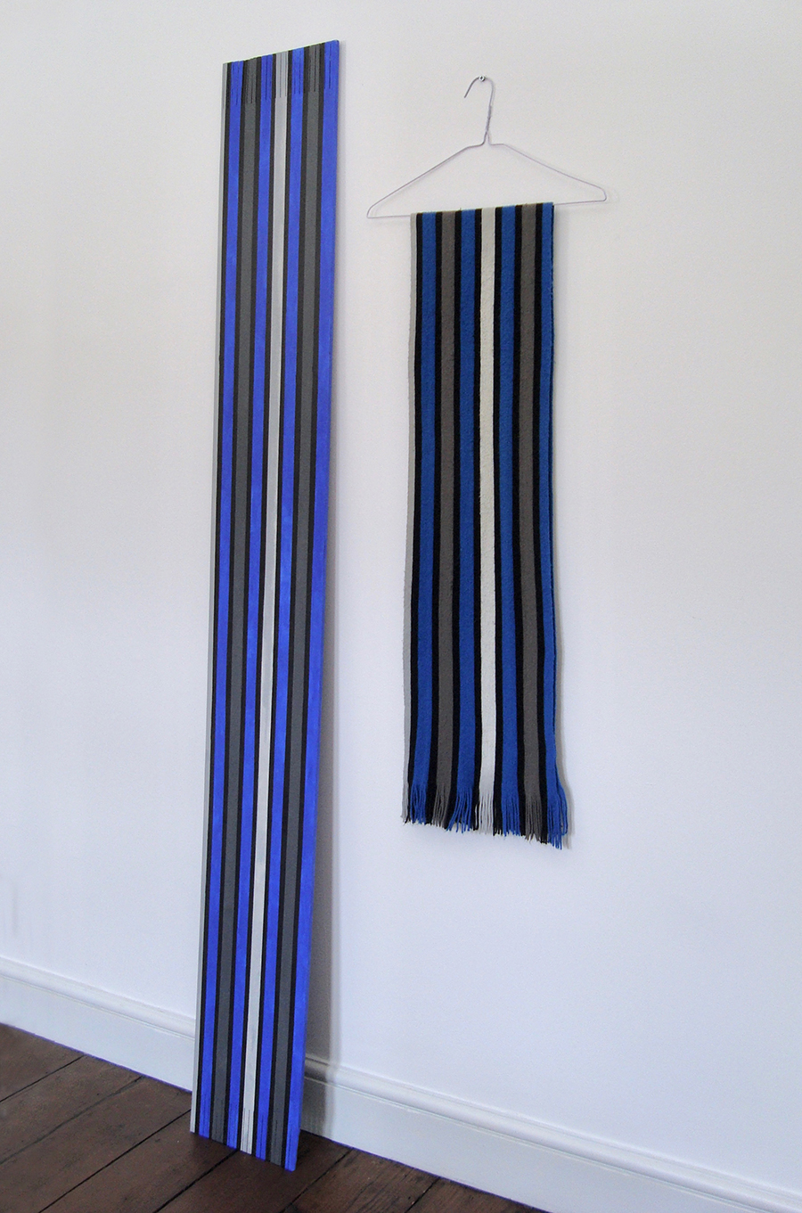A wooden art sculpture of a stripy blue scarf next to the original blue scarf